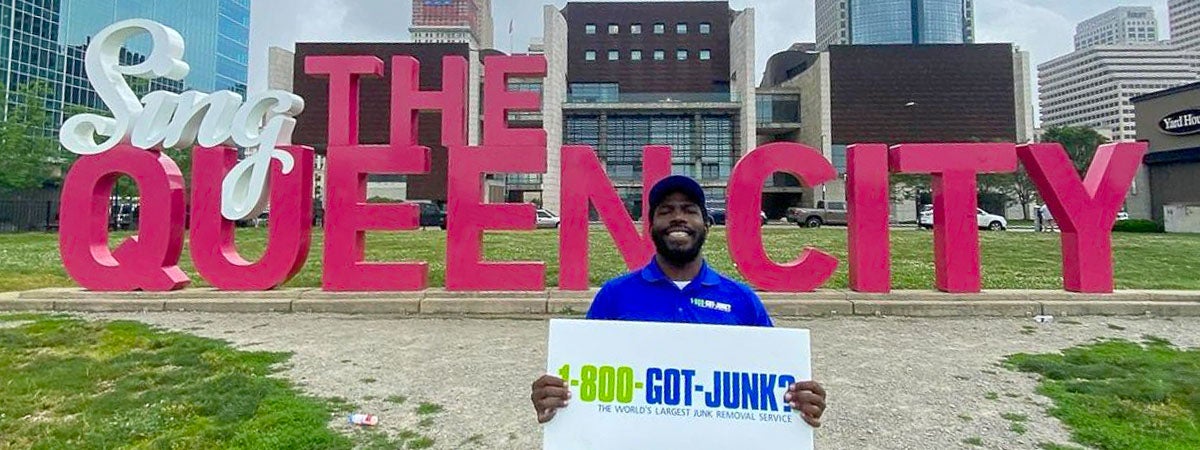 1-800-GOT-JUNK? Cincinnati team member standing at the Sing the Queen City sign in Freedom Park