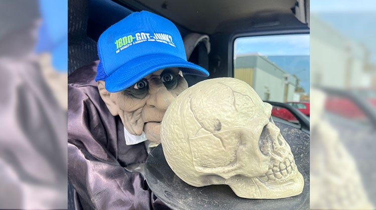 Halloween ghoul wearing a 1-800-GOT-JUNK? hat, holding a skull on a platter