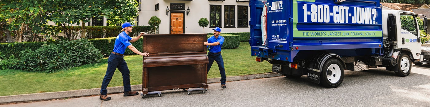 Two 1-800-GOT-JUNK? team members picking up a piano for removal and donation