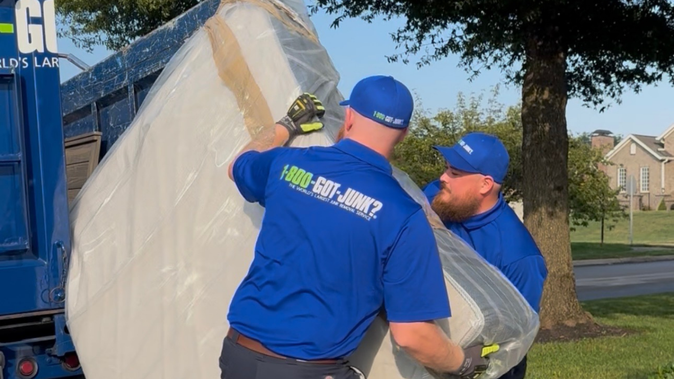 Two 1-800-GOT-JUNK? Truck Team Members lifting a mattress into the truck.