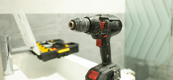 A screwdriver removing nails securing a tub to studs.