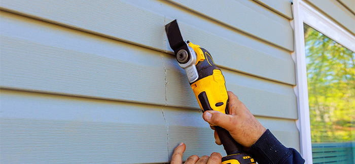 A person repairing damaged vinyl siding on a home.