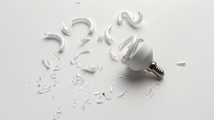 A broken CFL bulb with glass shards spread across white tabletop