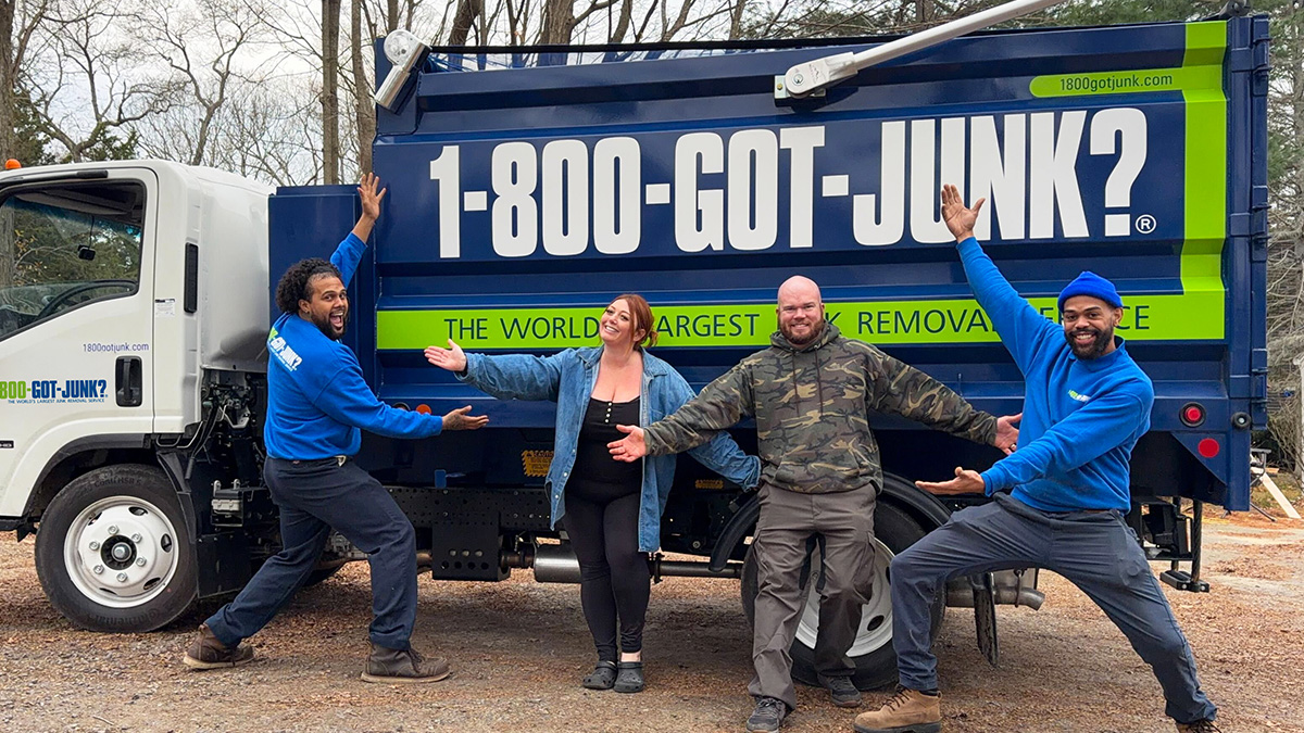 A woman and man with two 1-800-GOT-JUNK? Truck Team Members smiling in front of the truck.