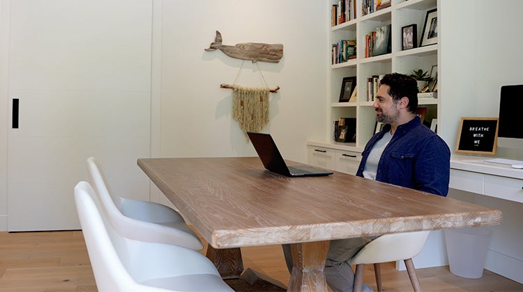 Man sitting at table with laptop in a clean, organized room