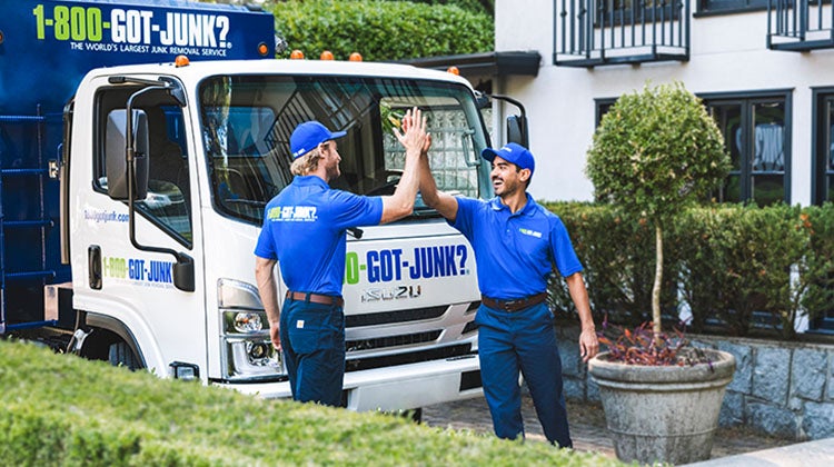 1-800-GOT-JUNK? truck team members in front of truck high-fiving outside of a home