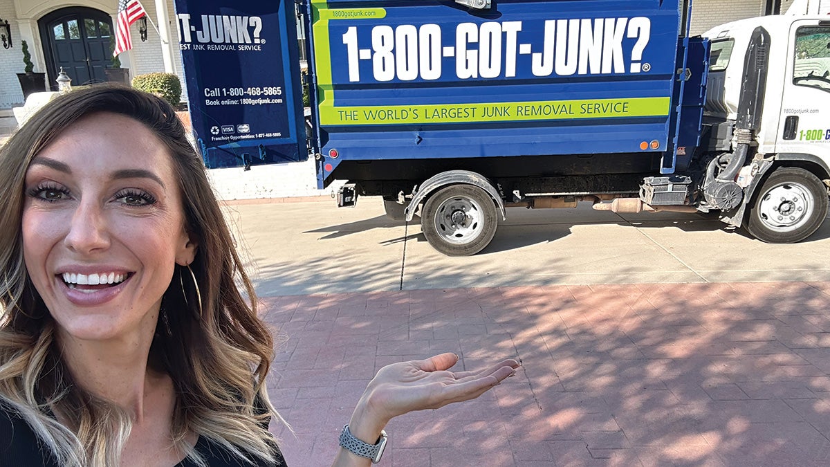 Jordan Page smiling while pointing at a 1-800-GOT-JUNK? truck parked outside her house