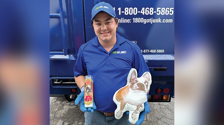 1-800-GOT-JUNK? uniformed truck team member holding a pillow in the shape of a french bull dog