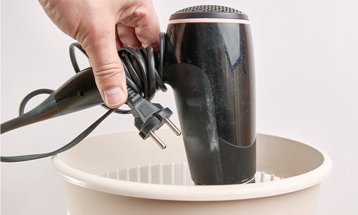 Hand holding an outdated hair dryer over a white garbage can