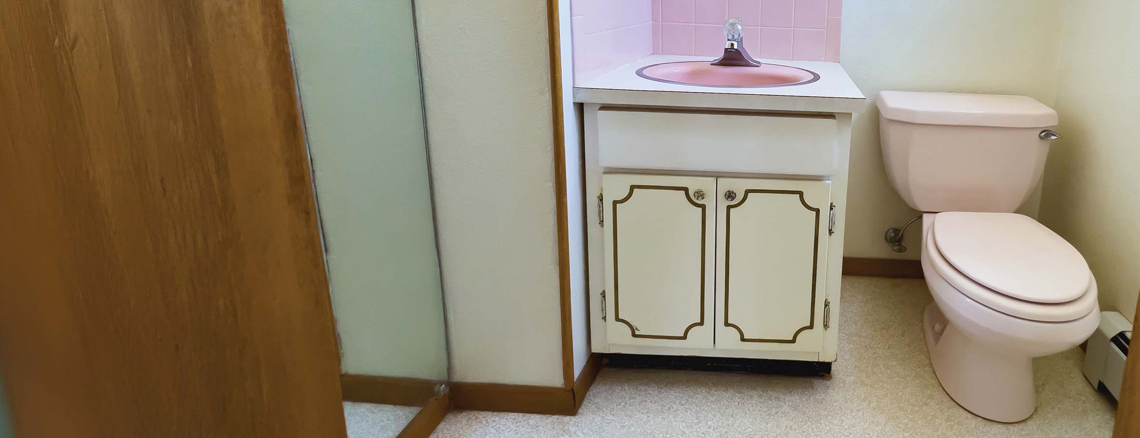 Toilet in an outdated bathroom next to an old vanity