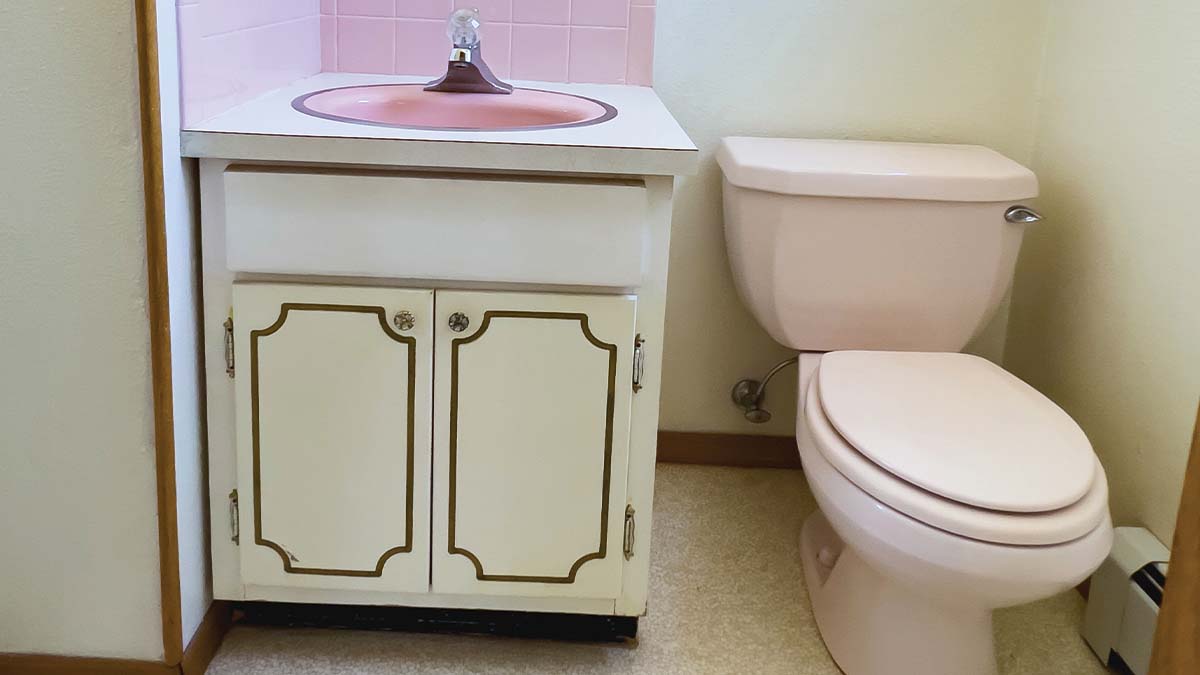 Toilet in an outdated bathroom next to an old vanity