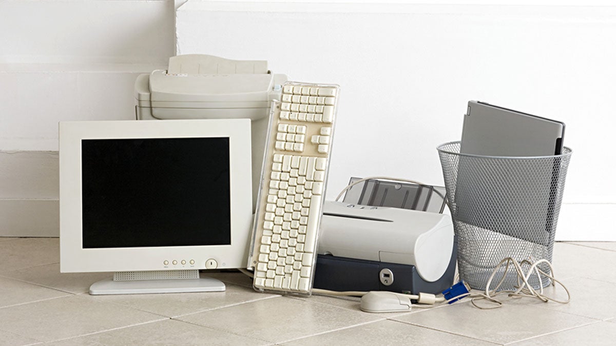 pile of outdated electronics: computer monitor, keyboard, printer, paper shredder, laptop and wire waste paper basket