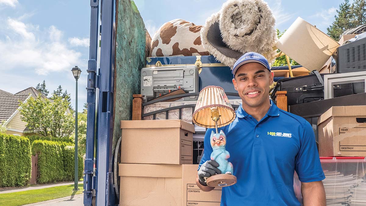 1-800-GOT-JUNK? team member holding a lamp behind a truck containing rolled up carpet among other items