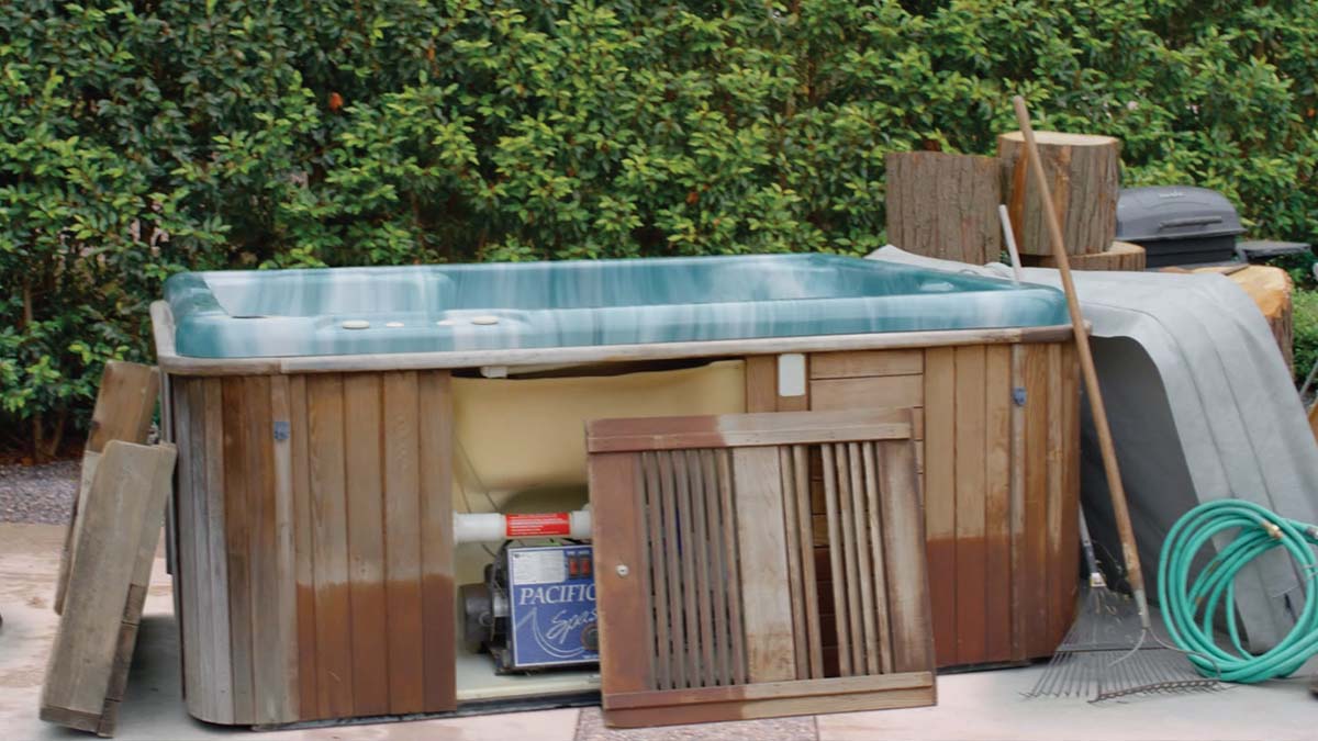 Old drained hot tub in residential yard with side panel removed 