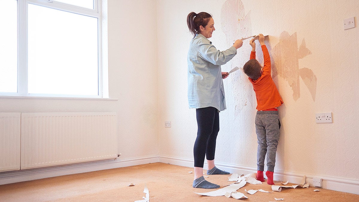 A mother and son face a wall while removing wallpaper