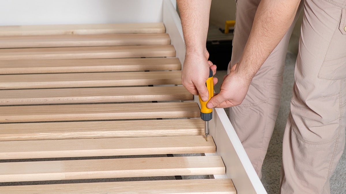 Person using yellow screwdriver to remove wooden bedframe slats