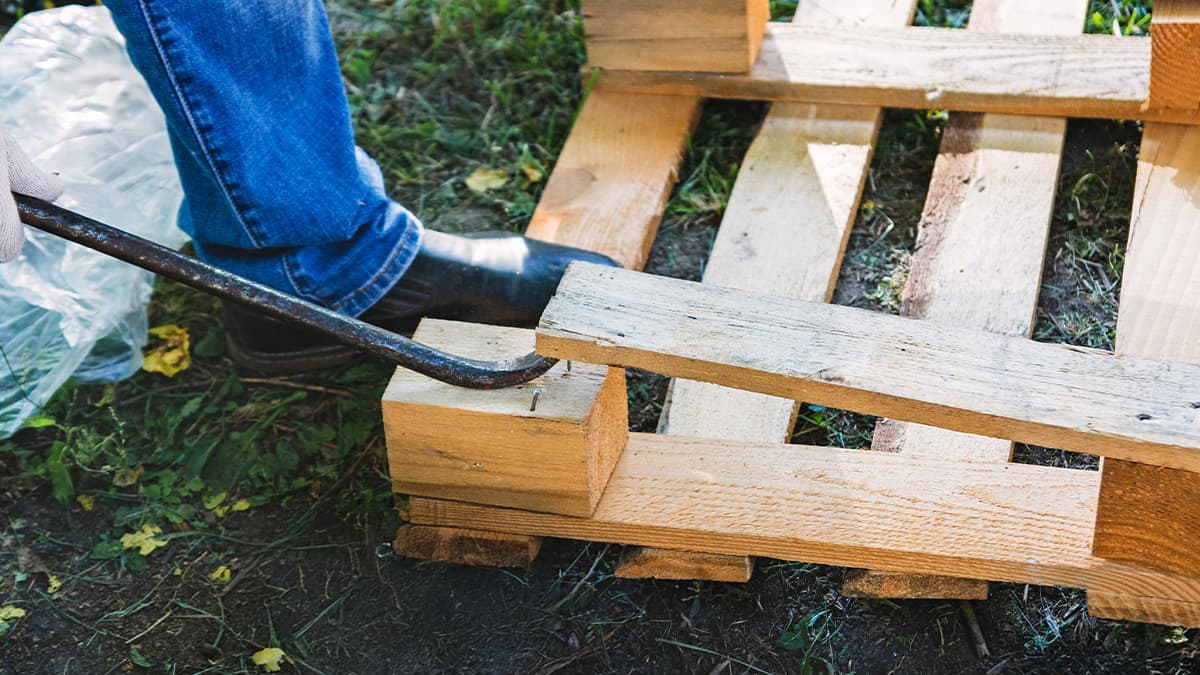 Person stepping on pallet to take it apart with crowbar